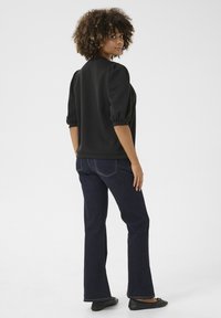 Svart sweatshirt med puffärmar, kombinerad med mörkblå utsvängda jeans. Modellen bär svarta lägenheter och står framför en enkel bakgrund.