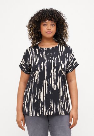 Haut à motifs noir et crème avec des manches courtes et un col rond. Le tissu a une texture lisse avec un design de coups de pinceau verticaux.