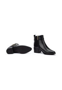 Botines de cuero negro hasta el tobillo con puntera puntiaguda y tacón cuadrado. Presentan una cremallera lateral y detalles de correas decorativas. Suela de goma con patrón antideslizante.