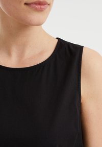 Schwarzes ärmelloses Oberteil aus Baumwolle. Rundhalsausschnitt mit Stickdetail, das die glatte Textur und das schlichte Design hervorhebt.