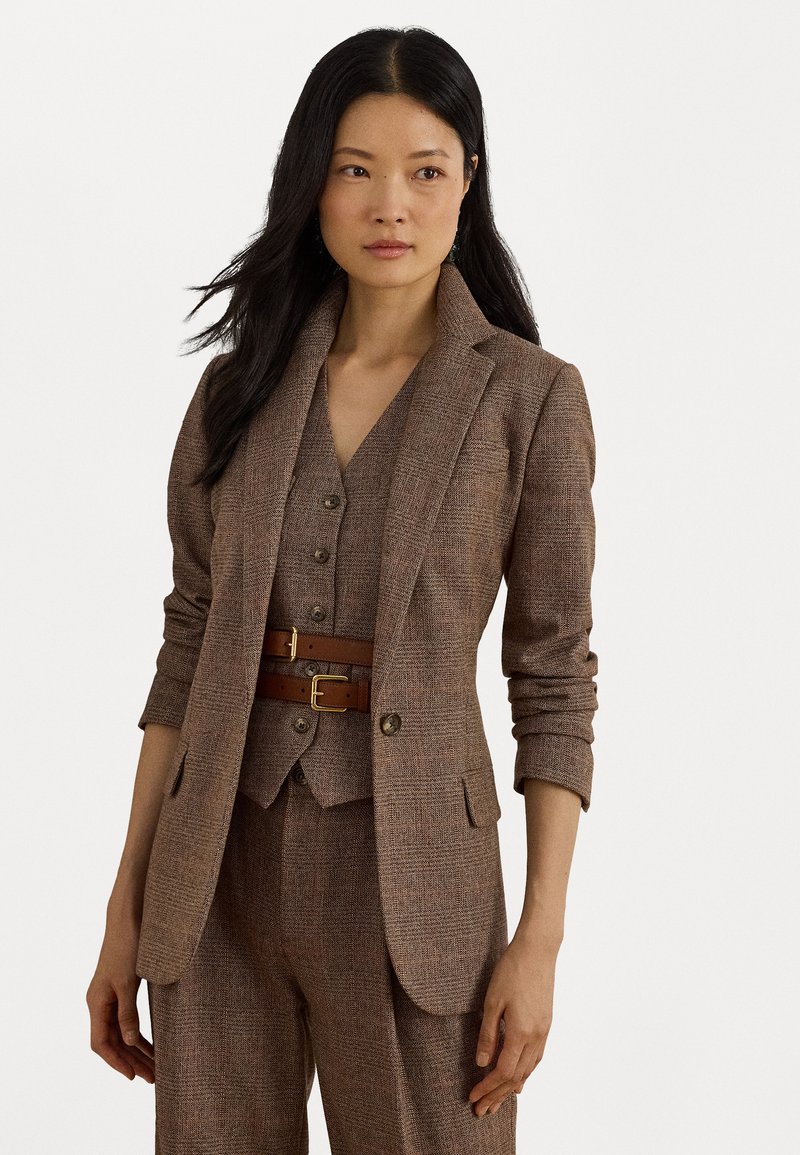 Ruskea teksturoitu bleiseri, jossa on leikkaamalla muotoiltu kaulus, yhdistettynä matching-vyöhykkeeseen ja housuihin. Korostettu ruskealla nahkavyöllä, jossa on kultaiset soljet.