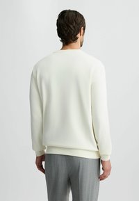Crème-kleurige sweatshirt met lange mouwen, ronde hals en geribde manchetten. Het is gemaakt van een gladde stof met een relaxte pasvorm.