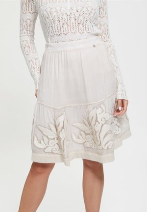 Knee-length embroidered skirt in light cream, yang menampilkan aksen bunga berpola, tekstur lipit, dan desain kain yang lembut dan transparan.