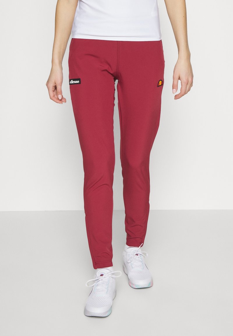 Röda träningsbyxor med slim fit, gjorda av stretchigt material. Har logopatchar och en slät yta, i kombination med vita sneakers.