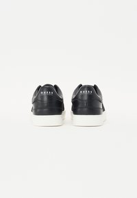 Sneaker in pelle nera con una texture liscia, suola in gomma bianca e dettagli del logo sul retro. Design rotondo con una silhouette a taglio basso.