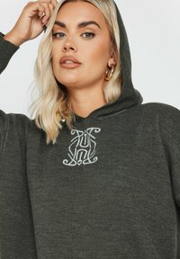 Mörkgrön huva tröja med en lös passform, med ett strukturerat tyg och en vit broderad design på bröstet.