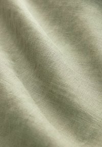 Svetlozelená látka s jemnou textúrou. Materiál sa zdá byť mäkký a mierne krčený, pričom predvádza jemný vzor tkania.