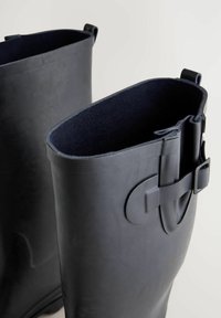 Zwarte rubberlaarzen met een gladde buitenkant, voorzien van een donkerblauwe stoffen voering en een zijgesp detail voor sluiting.