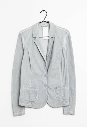 Hellgrauer Cordsakko mit zwei Frontknöpfen und aufgesetzten Taschen, aufgehängt an einem schwarzen Kleiderbügel vor weißem Hintergrund.