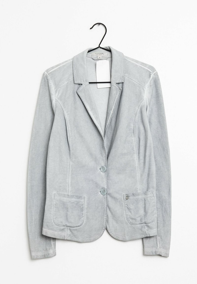 Blazer en velours côtelé gris clair avec deux boutons à l'avant et poches plaquées, suspendu sur un cintre noir devant un fond blanc.