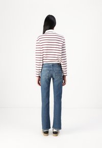 Striped long-sleeve shirt in white and burgundy, paired with blue denim jeans. Features relaxed fit, faded texture, and two back pockets.