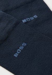 Mørkeblå sokker lavet af blødt stof, der har et struktureret design, med en lysblå "BOSS"-logo fremtrædende vist.