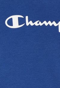 T-shirt di cotone blu con un grande logo bianco "Champion". Il tessuto ha una consistenza liscia con una leggera elasticità.