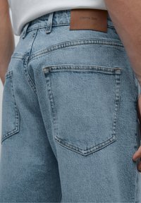 Light blue denim jeans with a classic fit, featuring two back pockets, subtle stitching details, and a brown leather brand label at the waistband.