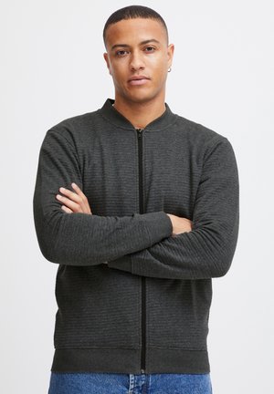 Tmavošedá bomber bunda na zips s rebrovanou textúrou, stojatým golierom a dlhými rukávmi. Má predný zips a priliehavý pás.