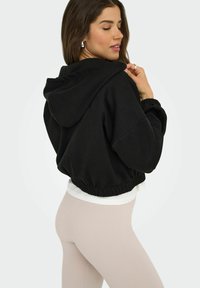 Un hoodie noir court avec une capuche à cordon, une ceinture élastique et des manches larges, associé à des leggings beiges clairs à côtes.