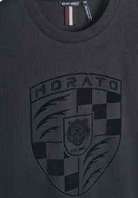 Crna pamučna majica s odvažno reljefnim tigrovim logotipom i dizajnom štita, s okruglim izrezom i kontrastnom prugastom oznakom.