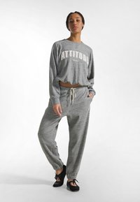 Sudadera gris recortada con el texto "ATTITUDE" en blanco, combinada con pantalones deportivos grises a juego que cuentan con cinturilla elástica y bolsillos laterales.