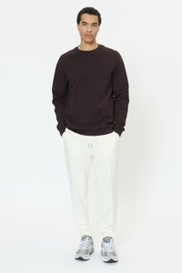 Temno rjava jopa z rebrastimi manšetami in pasom, kombinirana z belimi trenirkami z elastičnim pasom ter sivimi športnimi čevlji. Čist dizajn, sproščen kroj.