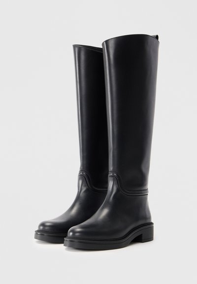 Botas negras hasta la rodilla de cuero suave. Punta redondeada, costuras mínimas, suela plana y un ligero tacón. Diseño simple y elegante.