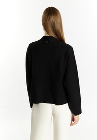 Zwarte wolmix sweater met een ontspannen pasvorm, raglan mouwen en een subtiele achterkant labeldetail, gecombineerd met crèmewitte broek.