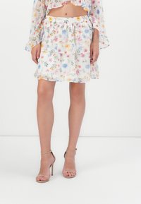 Jupe mini florale en tissu blanc translucide avec des motifs de fleurs colorées, dotée d'une taille élastique pour un ajustement confortable.