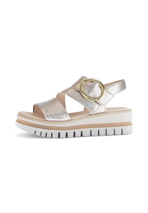 Metallic gold-colored sandal with crisscross straps, adjustable buckle, and a chunky white sole with textured grip. Elevated platform design.