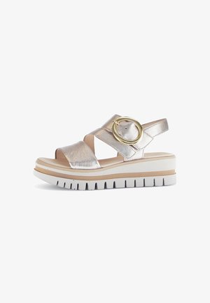 Metallic gold-colored sandal with crisscross straps, adjustable buckle, and a chunky white sole with textured grip. Elevated platform design.
