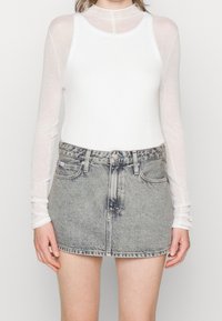 White long-sleeve top made of sheer material paired with a faded grey denim skirt featuring a straightforward cut and front pockets.