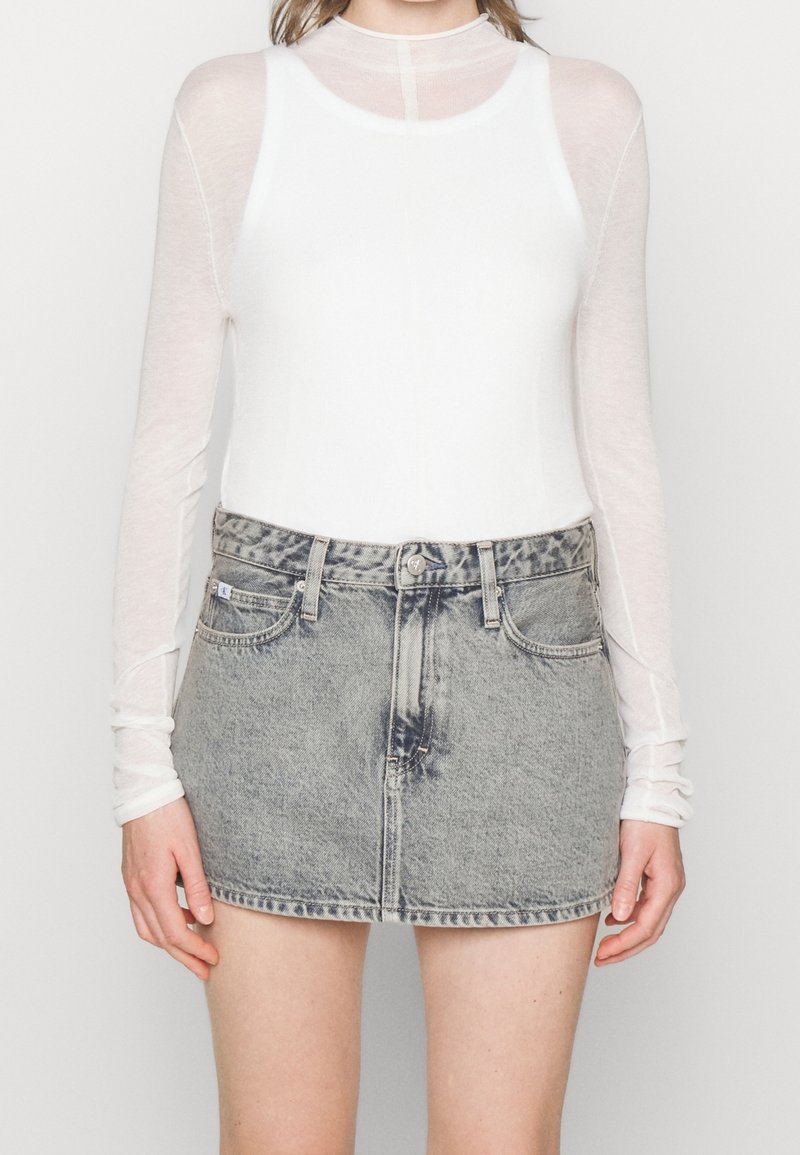 White long-sleeve top made of sheer material paired with a faded grey denim skirt featuring a straightforward cut and front pockets.