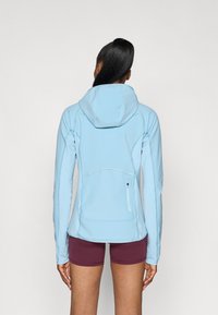 Casaco ajustado azul-claro, com uma superfície texturizada, capuz e um bolso com ziper na lateral; combinado com calções de cor bordô.