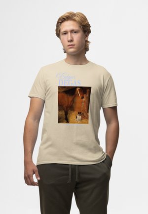 Jeune homme portant un t-shirt beige avec une œuvre d'Edgar Degas représentant un cheval brun et un petit chien noir et blanc dans un cadre d'écurie.