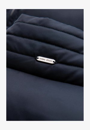 Niebieska kurtka puchowa z pikowanym wzorem, z metalową metką z napisem "OMBRE EXTIMO" oraz wzmocnionymi szwami.