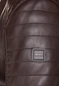 Brun läderjacka med kviltad axeltextur, med en fyrkantig logopatch med "BOSS" på svart bakgrund.