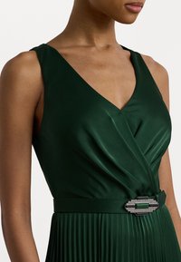 Grön satin klänning med V-ringning, veckad kjol och ett metallband med en dekorativ spänne med gröna och silver accenter.