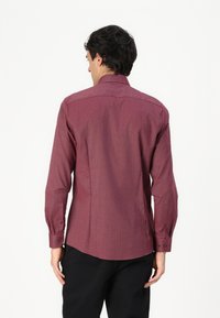 Chemise à manches longues bordeaux avec un motif texturé subtil, ourlet arrondi et poignets boutonnés. La vue de dos montre un col classique.