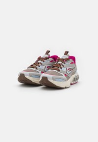 Grå och rosa sportskor med meshövre, bruna snören och texturerad gummisula. Anmärkningsvärda designakenter på sidorna och bakre delen.