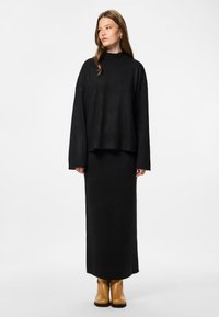 Črna rebrasta pletena jopica z visokim ovratnikom in dolgimi rokavi, v paru s črno rebrasto krilom, dopolnjena z rjavimi gležnjarji.