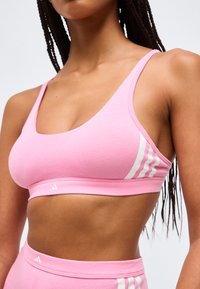 Γυναίκα που φοράει ροζ αθλητικό σουτιέν και αντίστοιχα σορτς με ψηλή μέση και λευκές ρίγες Adidas, εικονιζόμενη από το στήθος έως τη μέση.