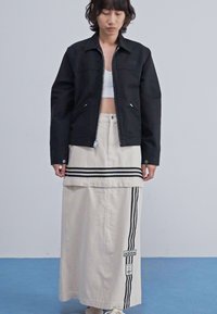 Must mustriga mustri jakk, millel on kaelus, koos heledast beežist seelikust, millel on mustad triibud ja Adidas logo plekk. Sile tekstuur, lõdva disainiga.