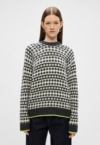 Pulover tricotat cu un model gri și alb, cu mâneci lungi și decolteu rotund, având un tiv și manșete de culoare verde neon.