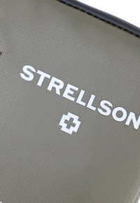 Izdelek Strellson z natančno strukturirano olivno zeleno površino, embosiranim belim logotipom in akcentom križnega simbola. Ima pravokotno obliko z gladkimi robovi.