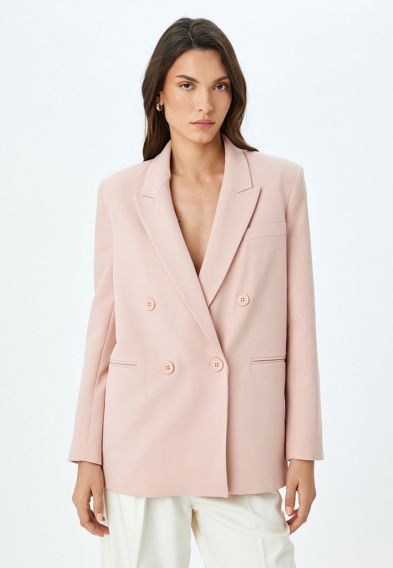 Doppelreiher-Blazer aus hellrosa Stoff, mit Reverskragen, seitlichen Taschen und einem lässigen Schnitt sowie einer Vierknopf-Verschluss.