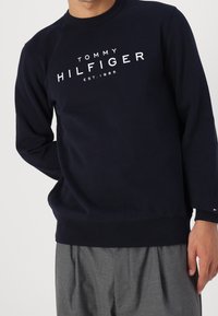 Sweatshirt en coton bleu marine avec des poignets et un ourlet côtelés ; arbore un grand logo blanc "TOMMY HILFIGER EST. 1985" à l'avant.