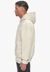 Helle beige Kapuzensweatshirt aus weichem Material; mit einer Kängurutasche und gerippten Bündchen. Angeschnittene Passform, keine sichtbaren Muster.