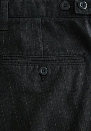 Mörkt randigt tyg med en knappad passpoalficka och två knappar längs midjan på ett skräddarsytt plagg.