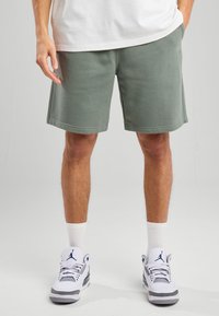 Green cotton shorts with a relaxed fit, featuring a smooth texture and solid color, paired with white socks and white sneakers.