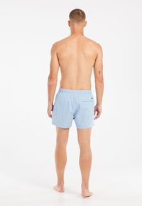 Svetlomodré plavky s elastickým pásom a zadnou vreckom, vyrobené z rýchloschnúceho materiálu. Zobrazené zozadu.