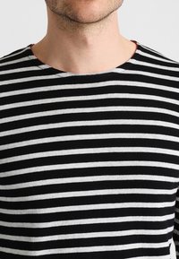 Chemise à manches longues à rayures noires et blanches avec un col rond. Le tissu semble doux et léger avec des rayures uniformes.