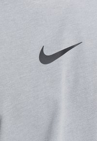 Camiseta gris de algodón suave, con un prominente logotipo negro de Nike en la parte frontal. Textura lisa con un diseño clásico de cuello redondo.